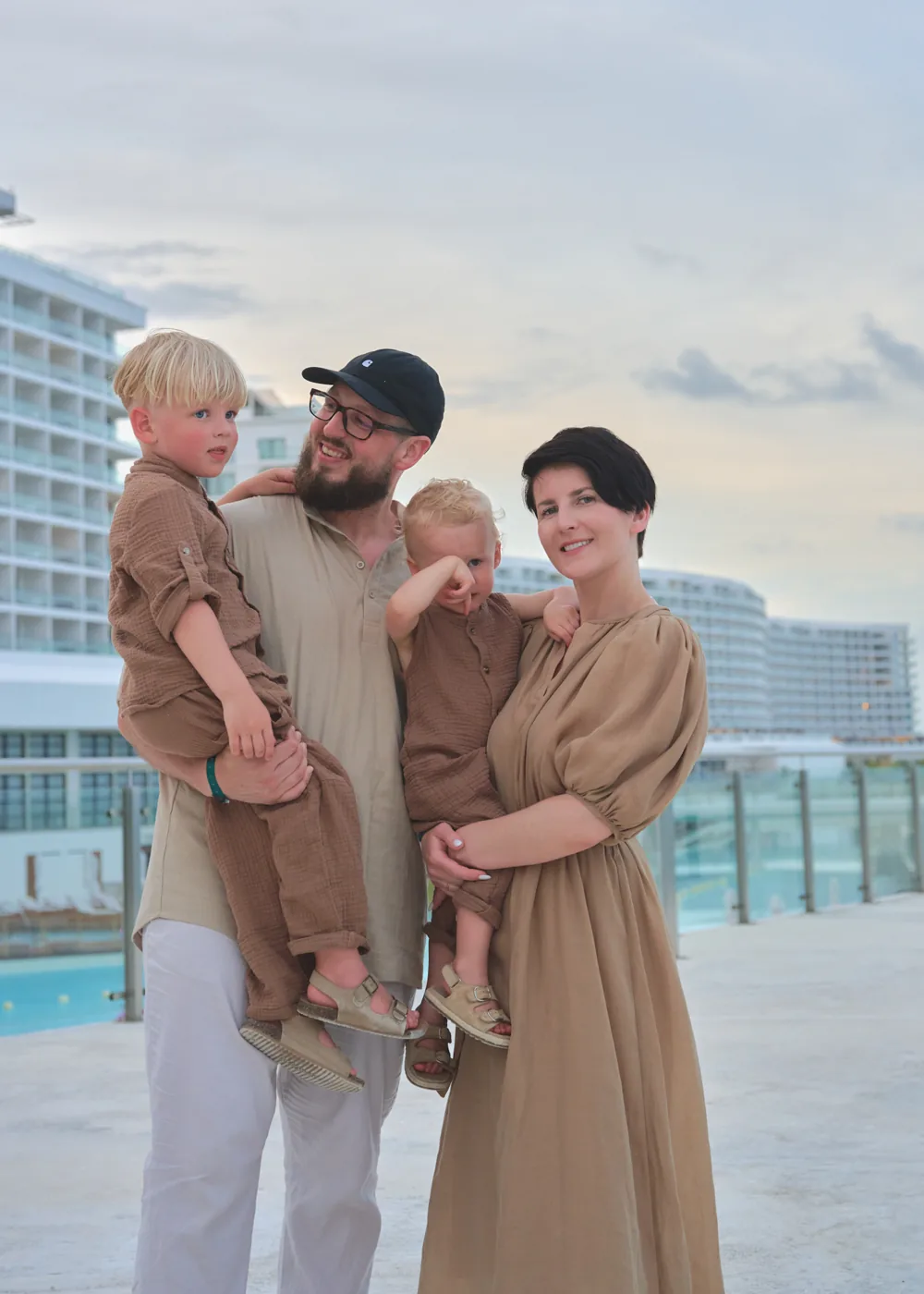 Marko holding one of his boys, Oksana beside him, resort pool deck behind them